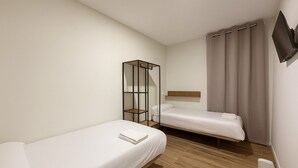 A small, clean room with two single beds, a wooden floor, a TV mounted on the wall, and a window with curtains. - Hostal Alcorcon (Alcorcón)