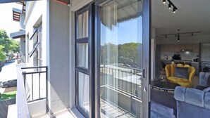 A modern apartment with a balcony, a sliding glass door, and a kitchen visible through the door.