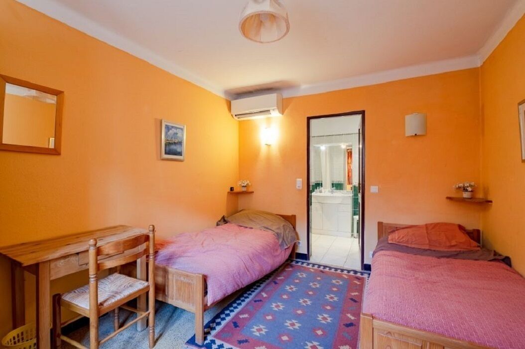 A room with two beds, a desk, and a chair. There is a door leading to a bathroom.