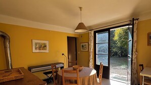A dining area with a round table, chairs, and a piano. There is a door leading outside, and the walls are painted yellow.