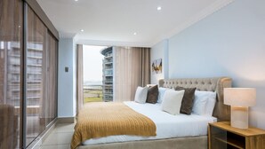 A modern hotel room with a large bed, a nightstand, a lamp, and a view of a building through the window.