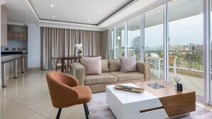 A modern living room with a sofa, armchair, and coffee table, a dining area with a table and chairs, and a kitchen with stainless steel appliances.