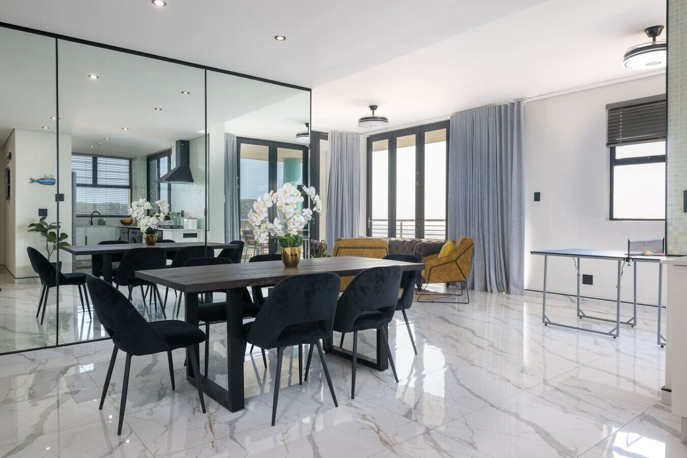 Un espace repas moderne avec un sol en marbre, une cloison en verre et une vue sur la cuisine.