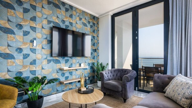 Ein modernes Wohnzimmer mit großem Fernseher, bequemen Sitzgelegenheiten, einem Holztisch und Meerblick durch eine Glastür.