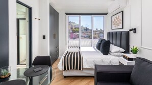 A modern bedroom with a large bed, a desk, a chair, and a balcony with a city view. - 602 The Valour Luxurious Apartment (Cape Town)