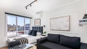 A modern bedroom with a large bed, a black sofa, a glass coffee table, and a city view through large windows. - 602 The Valour Luxurious Apartment (Cape Town)