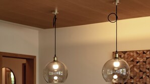 Un comedor con una mesa de madera dispuesta para cuatro personas, dos lámparas colgantes y una obra de arte geométrica en la pared.