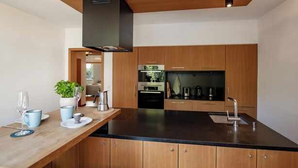 Una cocina moderna con armarios de madera, encimera negra y electrodomésticos de acero inoxidable.