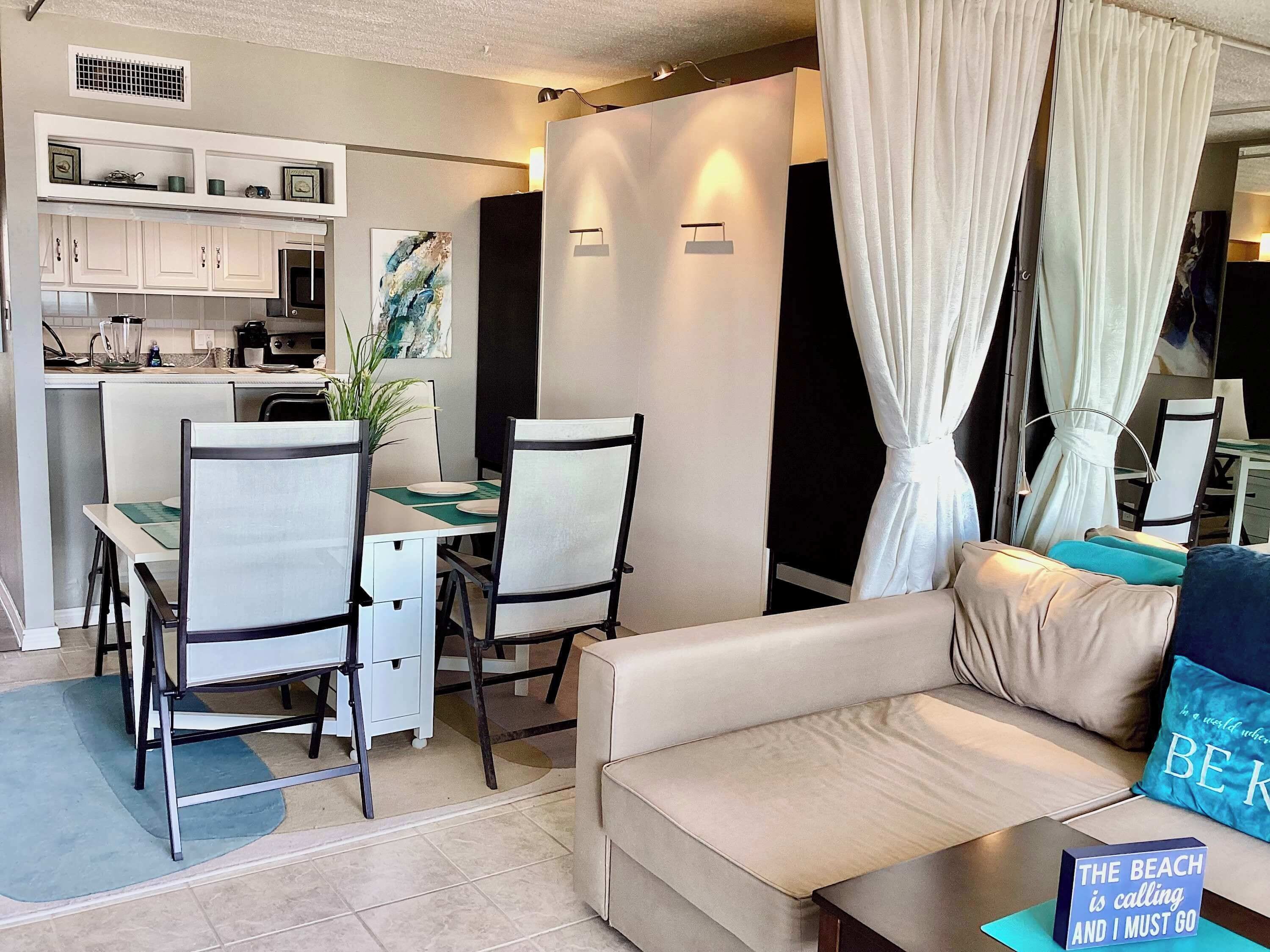 Una sala de estar moderna con sofá, mesa de comedor, sillas y una zona de cocina al fondo.