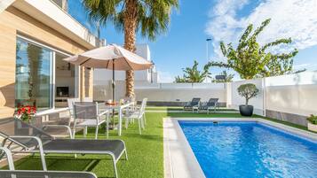 A modern outdoor pool area with a dining setup, lounge chairs, and a palm tree.