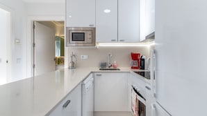 Een moderne keuken met witte kasten, een ingebouwde magnetron, een koffiezetapparaat en een vaatwasser.