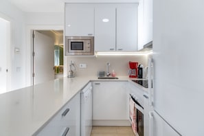 A modern kitchen with white cabinetry, a built-in microwave, a coffee maker, and a dishwasher.