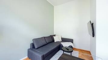 A modern living room with a grey sectional sofa, a small round coffee table, and a flat-screen TV mounted on the wall.