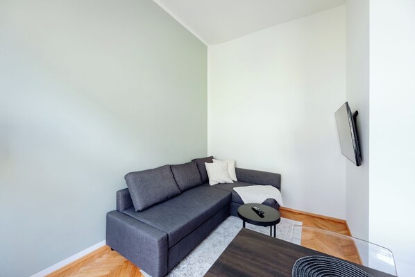 A modern living room with a grey sectional sofa, a small round coffee table, and a flat-screen TV mounted on the wall. - GH Luxury Apartments Graz, Gösser Haus (Graz)