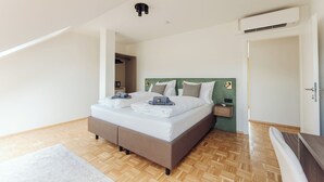 Quarto com uma cama grande, mesa de cabeceira, um criado-mudo e cabeceira verde, além de um aparelho de ar condicionado.