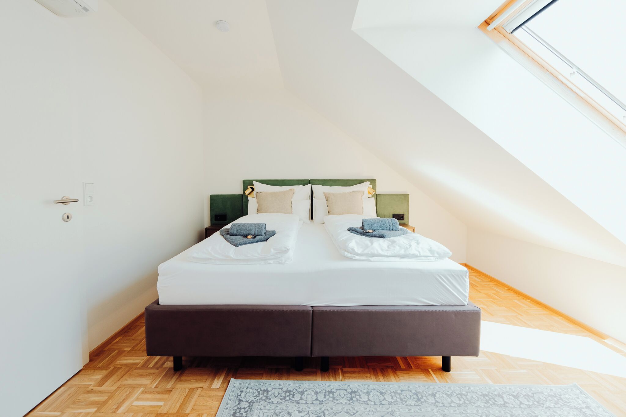 Ein modernes Schlafzimmer mit einem großen Bett, einem Oberlicht und einem Fischgrätparkett.