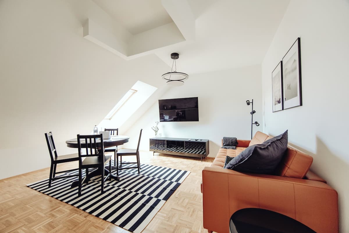 Un salon moderne avec un coin repas, comprenant un canapé, un téléviseur fixé au mur et un plancher en bois.