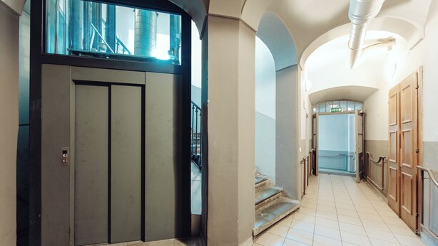 Corredor com elevador moderno, escada e vista para o exterior.