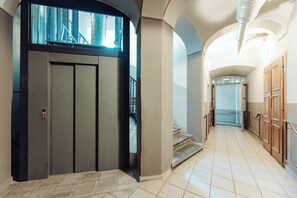 Un pasillo con un ascensor moderno, una escalera y vistas al exterior.