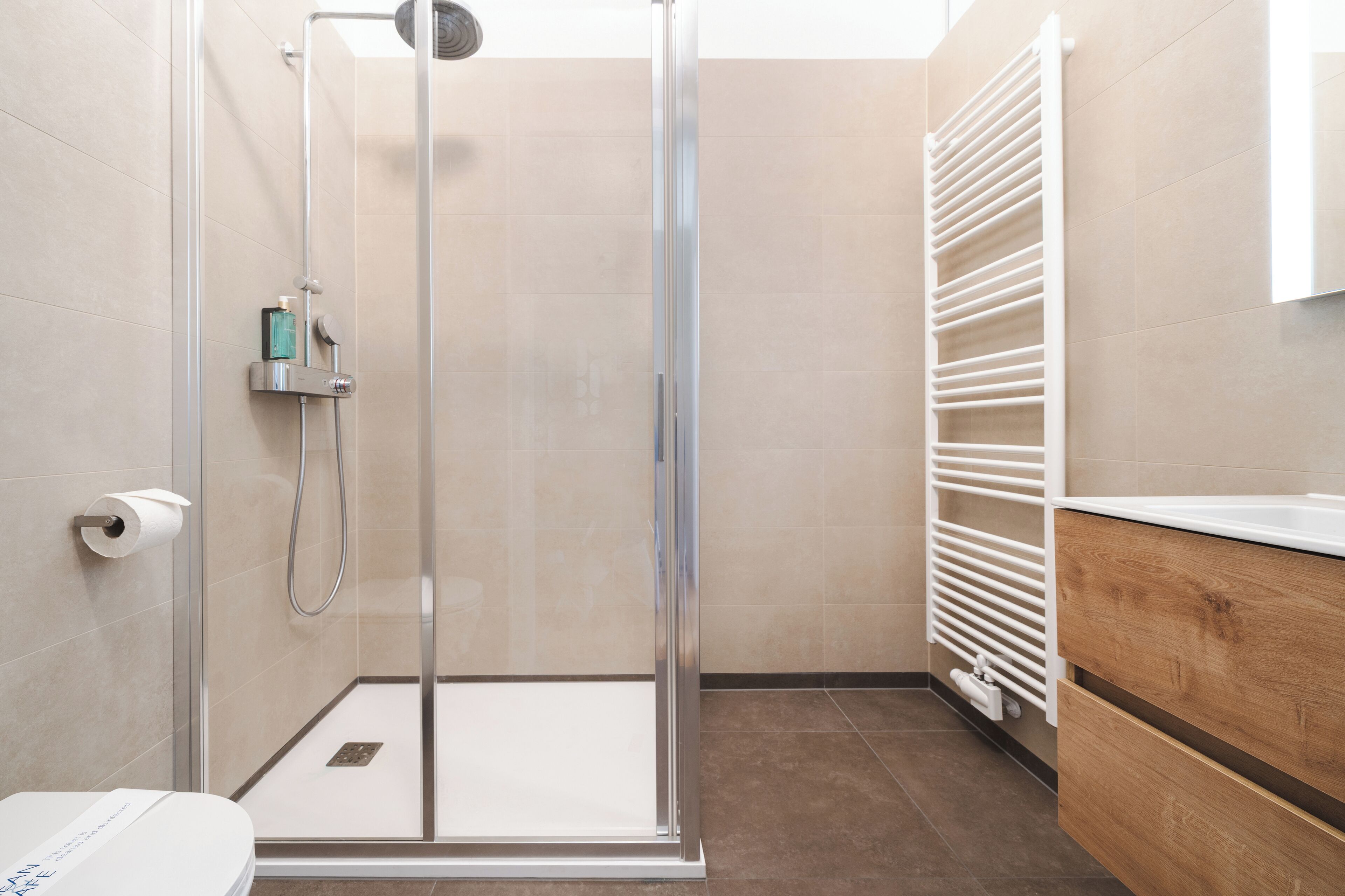 A modern bathroom with a glass-enclosed shower, a toilet, and a white towel rack.