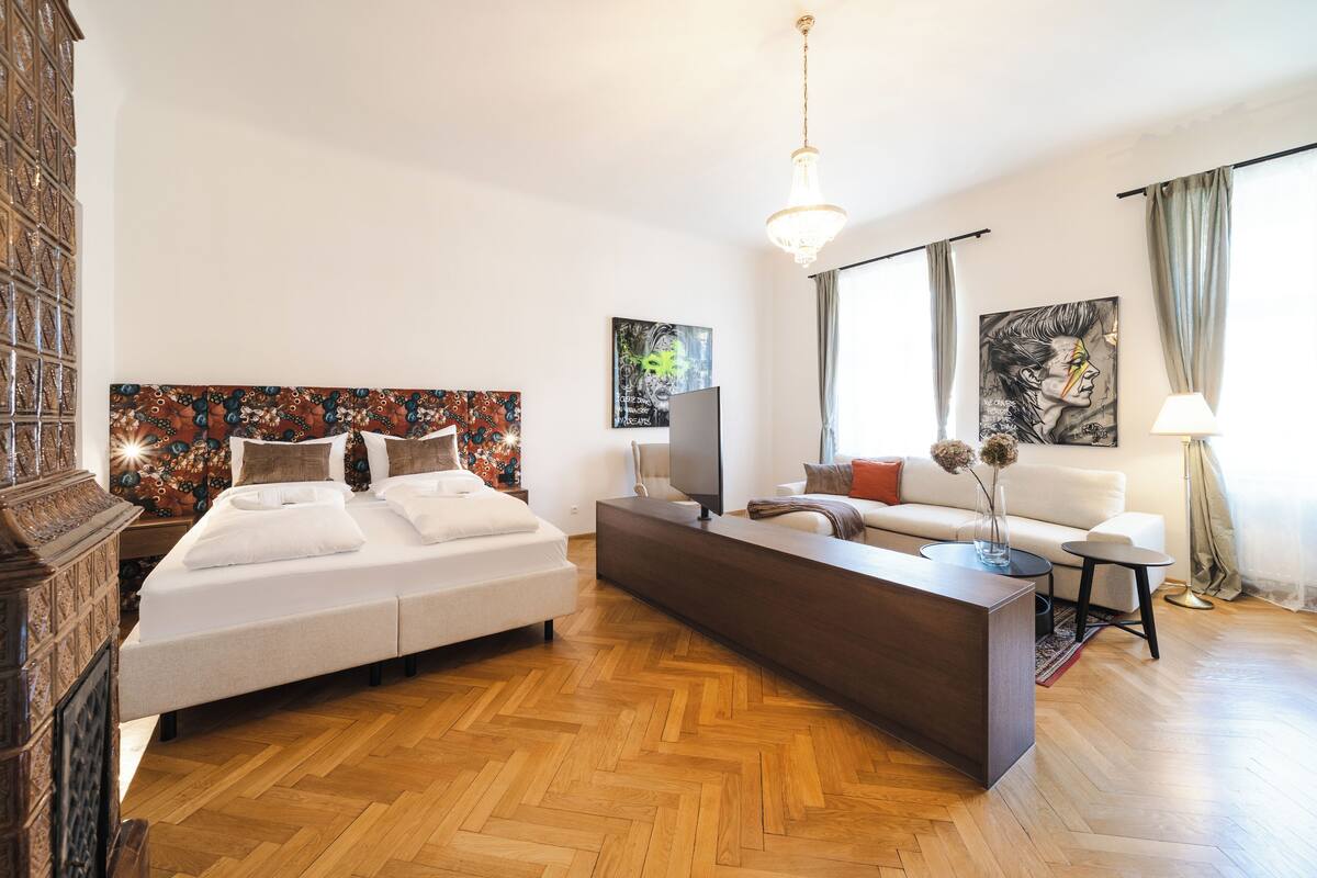 Une chambre d’hôtel moderne avec un grand lit, un parquet en bois disposé en chevrons, un canapé, une télévision et des œuvres d’art accrochées aux murs.