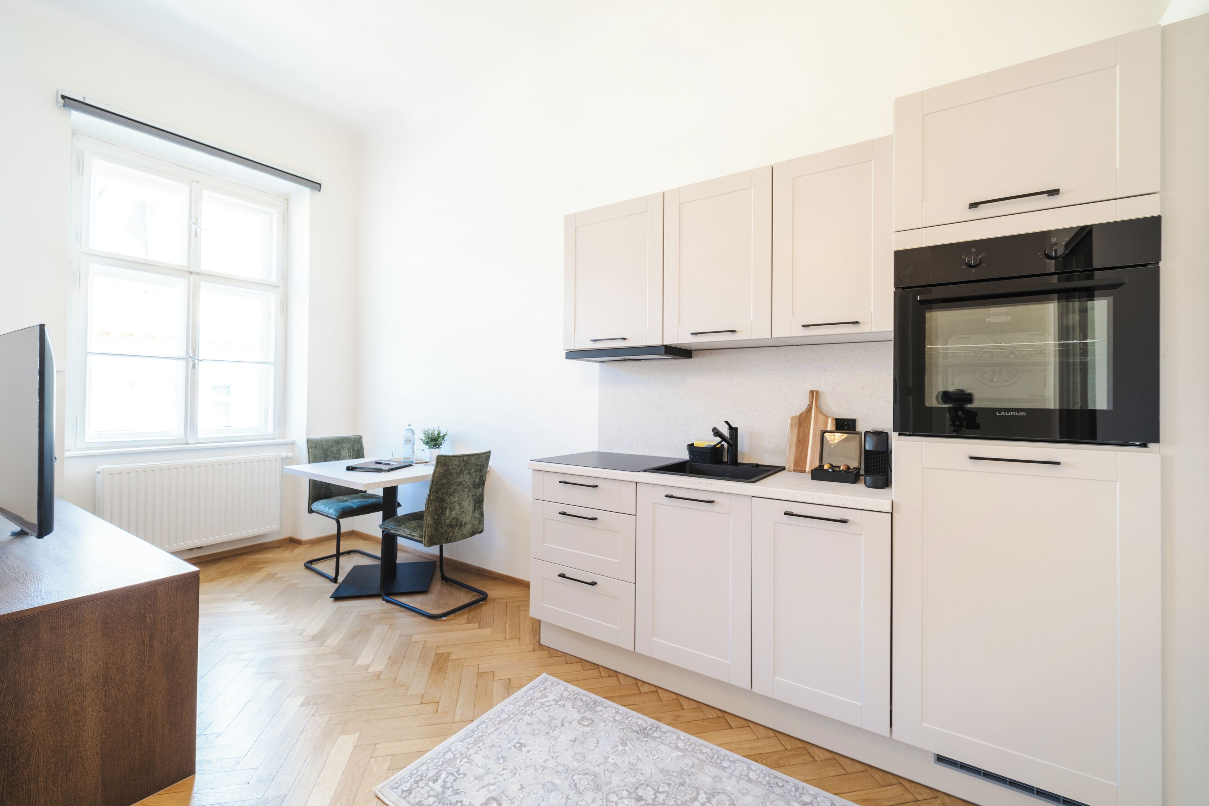 Una cocina moderna con armarios blancos, un horno negro y una zona de comedor con mesa y sillas.