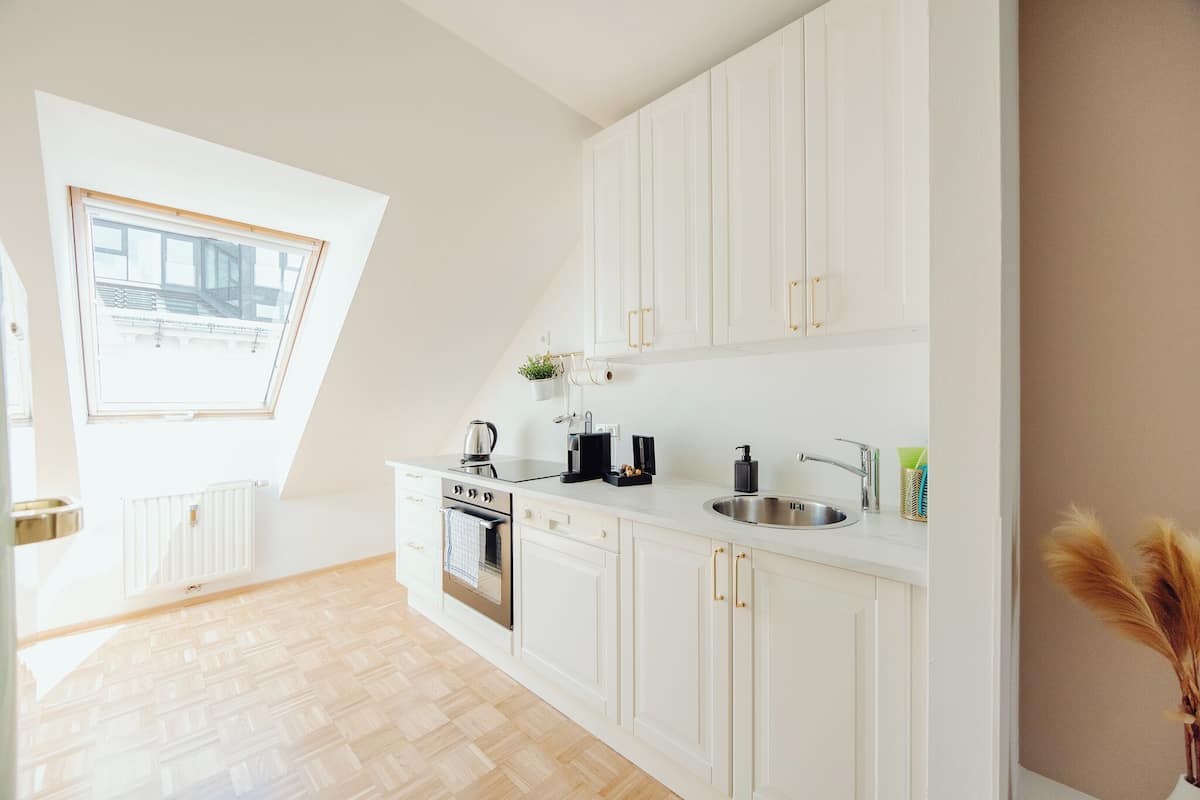 Une cuisine moderne avec des meubles blancs, un four encastré et une fenêtre au-dessus de l’évier.