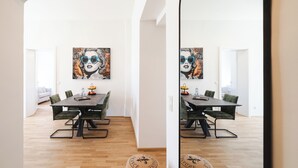 Uma sala de jantar moderna com piso de madeira, uma mesa preta e cadeiras estofadas em verde. Um quadro grande está pendurado na parede atrás da mesa.