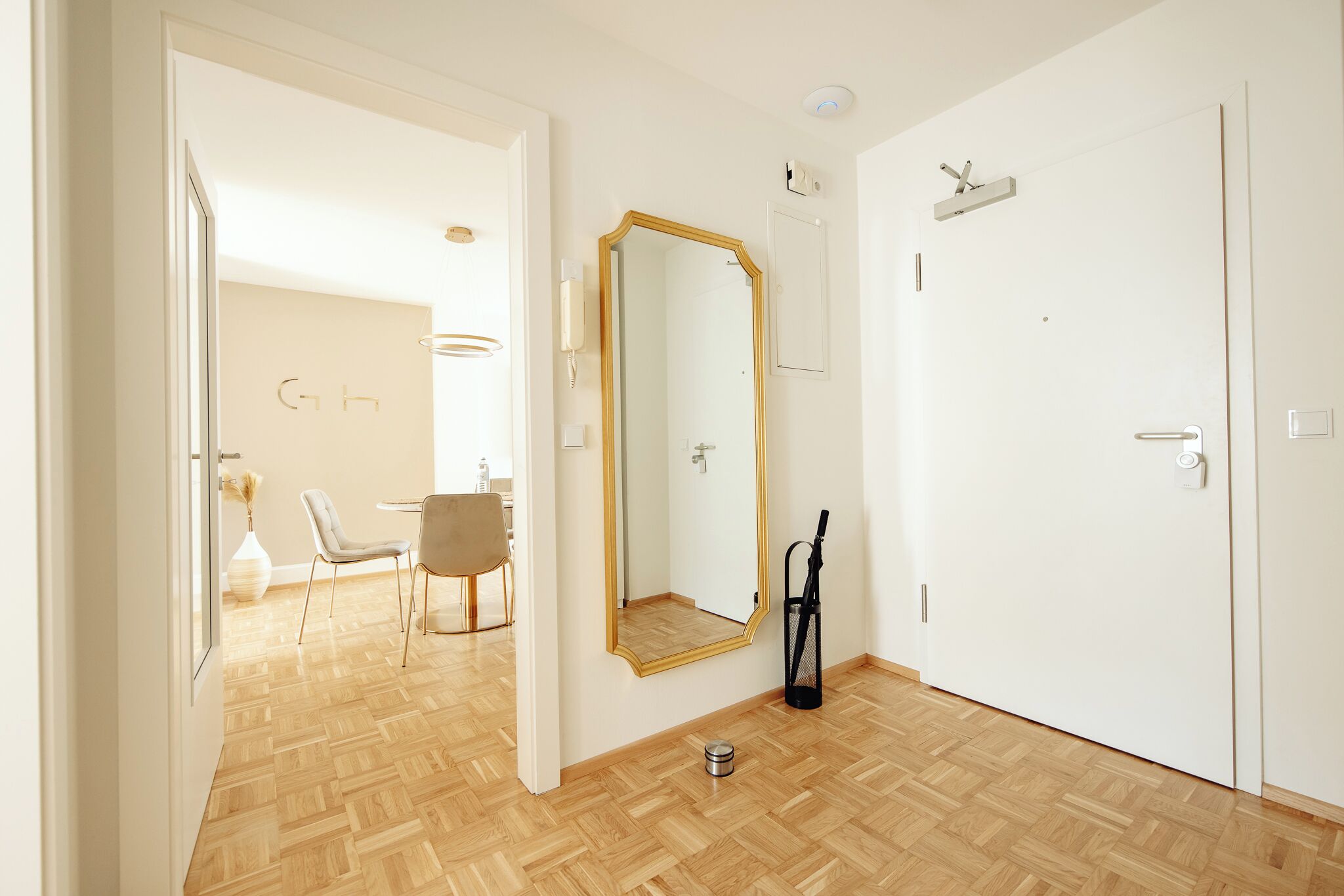 A room with a wooden parquet floor, a white door, a mirror with a gold frame, and a chair.