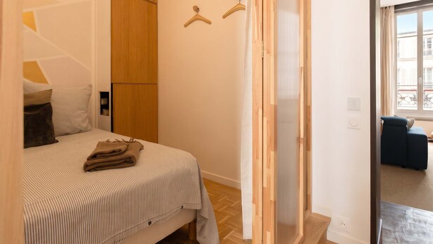 Un dormitorio con una cama, un armario de madera, perchero y vistas a un balcón.