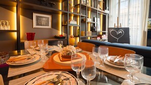 Comedor con una mesa dispuesta para una comida, rodeado de estantes con diversos objetos.