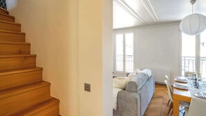 A wooden staircase leading to a living area with a sofa, dining table, and a view of the outdoors. - 6 Guests Duplex - Martyrs Village with view (Paris)