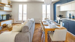 A modern living room with a sofa, dining table set for four, and a kitchen area with cabinets and appliances. - 6 Guests Duplex - Martyrs Village with view (Paris)