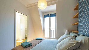 A bedroom with a bed, a window with curtains, a door, and a shelf with a lamp. - 6 Guests Duplex - Martyrs Village with view (Paris)