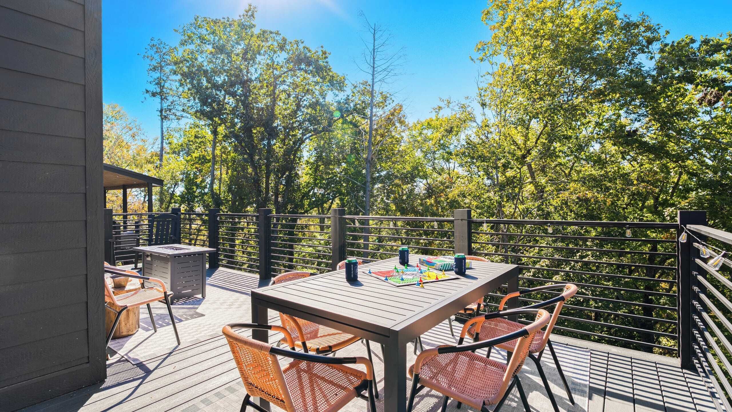 An outdoor deck with a table and chairs, surrounded by a metal railing and trees.