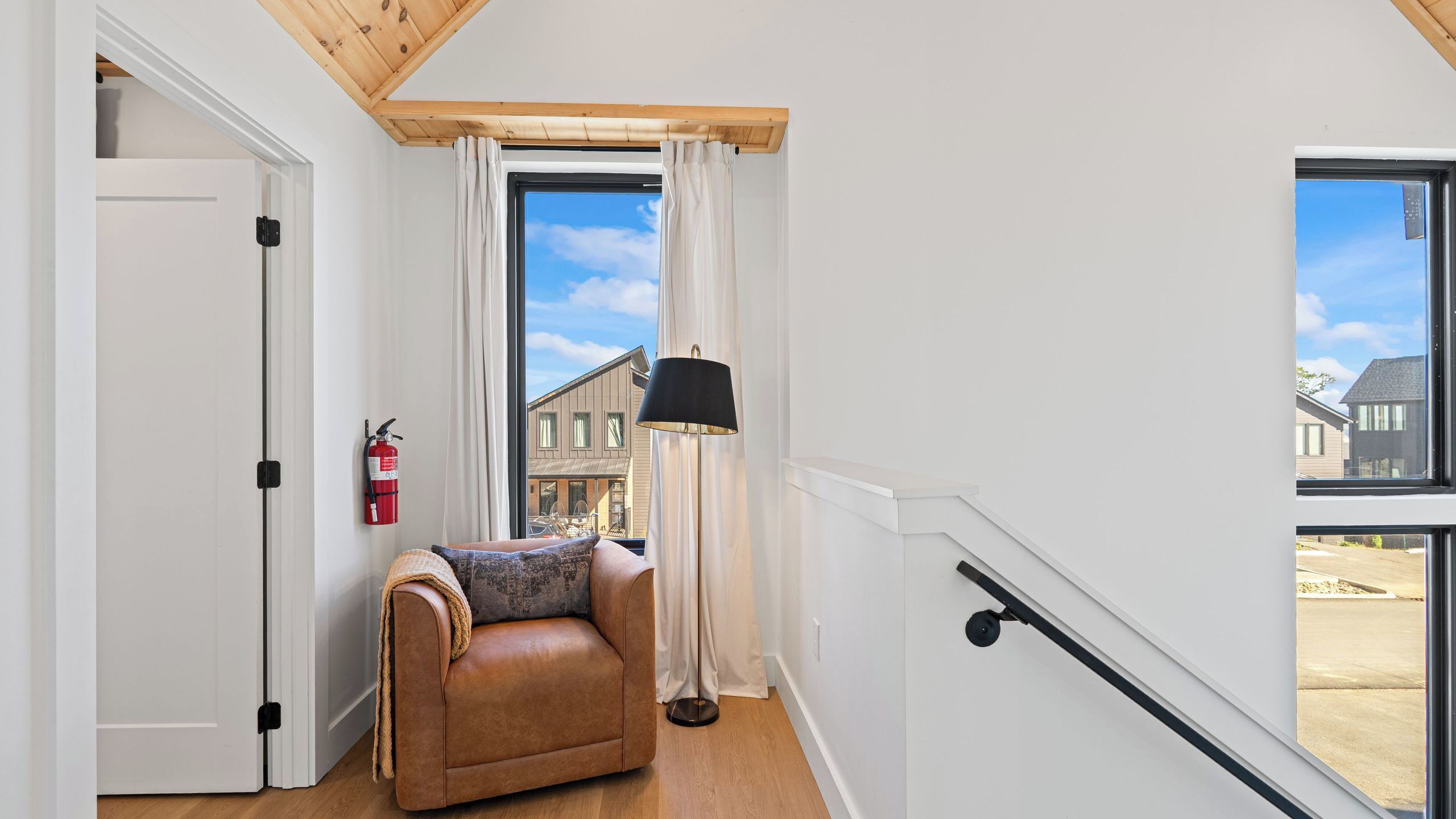 A room with a leather sofa, a fire extinguisher, a lamp, and a view of buildings outside.