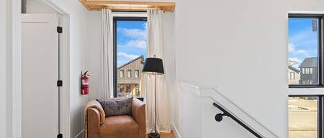 A room with a leather sofa, a fire extinguisher, a lamp, and a view of buildings outside.