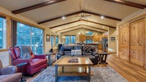 A spacious living room with a fireplace, leather sofas, a coffee table, and large windows offering a view of the outdoors.
