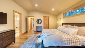A bedroom with a large bed, a dresser, a mirror, and a window with a view.