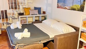Ett sovrum med en säng, en bänk, ett skrivbord, en stol, en trappa och en målning som föreställer ett landskap.