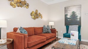 A living room with a red sofa, two lamps, a painting, and a teal armchair.
