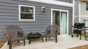 A house exterior with two wicker chairs, a small table, and a grill.