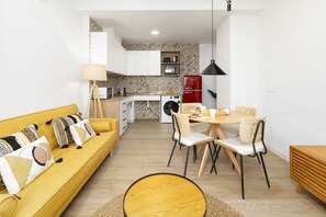 A modern living space with a yellow sofa, dining table, and chairs, a kitchen area with a red refrigerator, and a patterned backsplash.