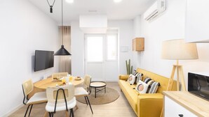 Un salon moderne avec un canapé jaune, une table à manger avec des chaises, un téléviseur et une lampe.