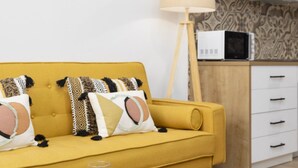 Un canapé jaune avec des coussins à motifs, un lampadaire et un four à micro-ondes posés sur un meuble en bois.