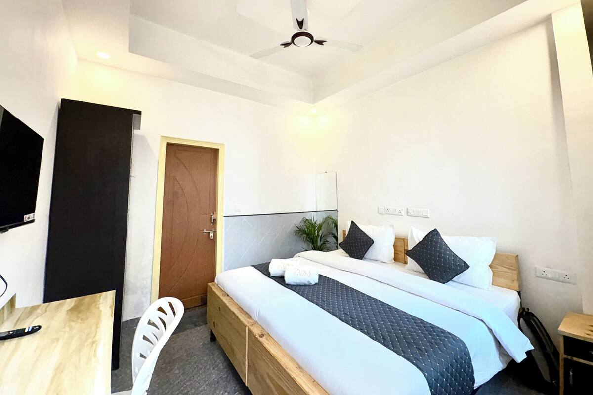 A modern hotel room with a large bed, a ceiling fan, a TV, and a wooden desk.
