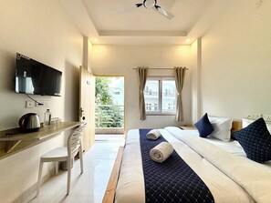 Une chambre d’hôtel avec un lit, un bureau avec une bouilloire, une chaise, une télévision et une fenêtre avec des rideaux.