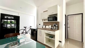 A modern kitchen with a microwave, toaster, and coffee maker. There is a bicycle parked outside and a table with a tissue box. - Baiyok Villas Near Kathu Waterfall (Kathu)