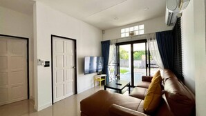 A modern living room with a sofa, a TV, and a sliding glass door leading to a balcony. - Baiyok Villas Near Kathu Waterfall (Kathu)