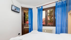 A hotel room with a bed, a television, a window with curtains, and a radiator. - Casa Daisy 2 by Rentbeat  (Limone)